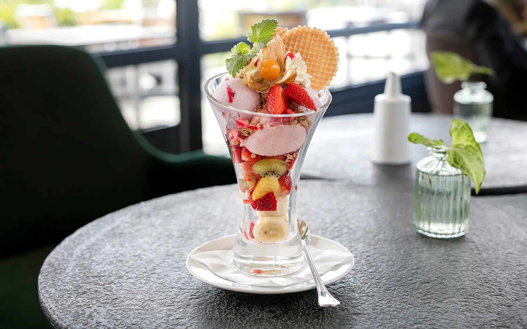 A colorful ice cream sundae with fresh fruits and a wafer on a table.