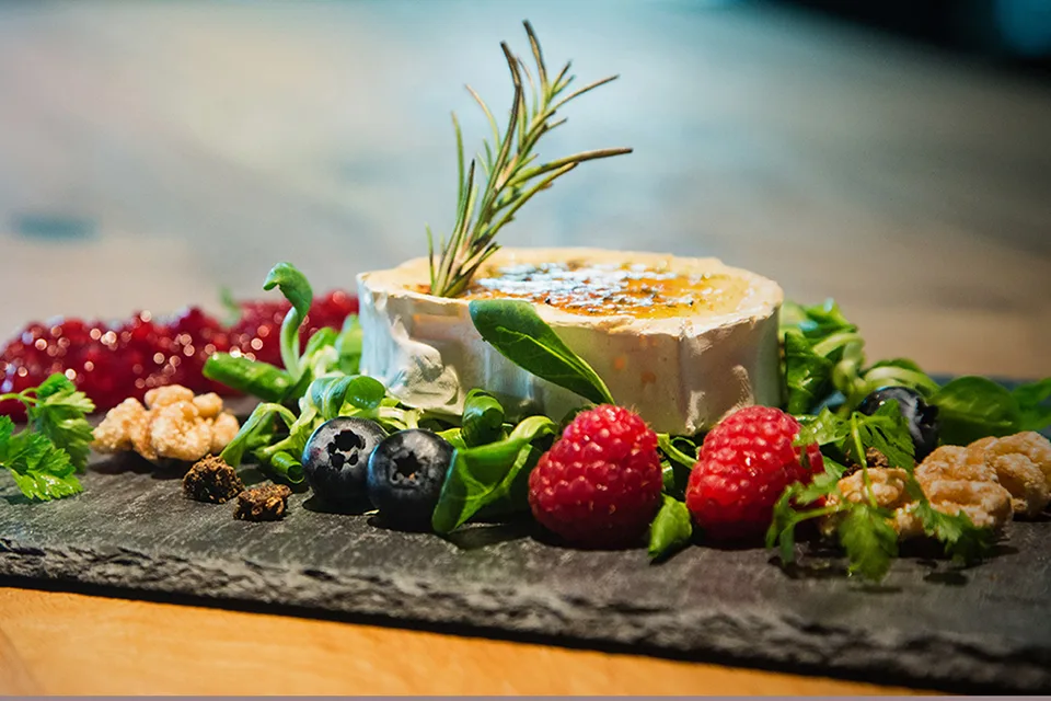 Eine Käseplatte mit frischen Beeren, Kräutern und einer süßen Sauce.