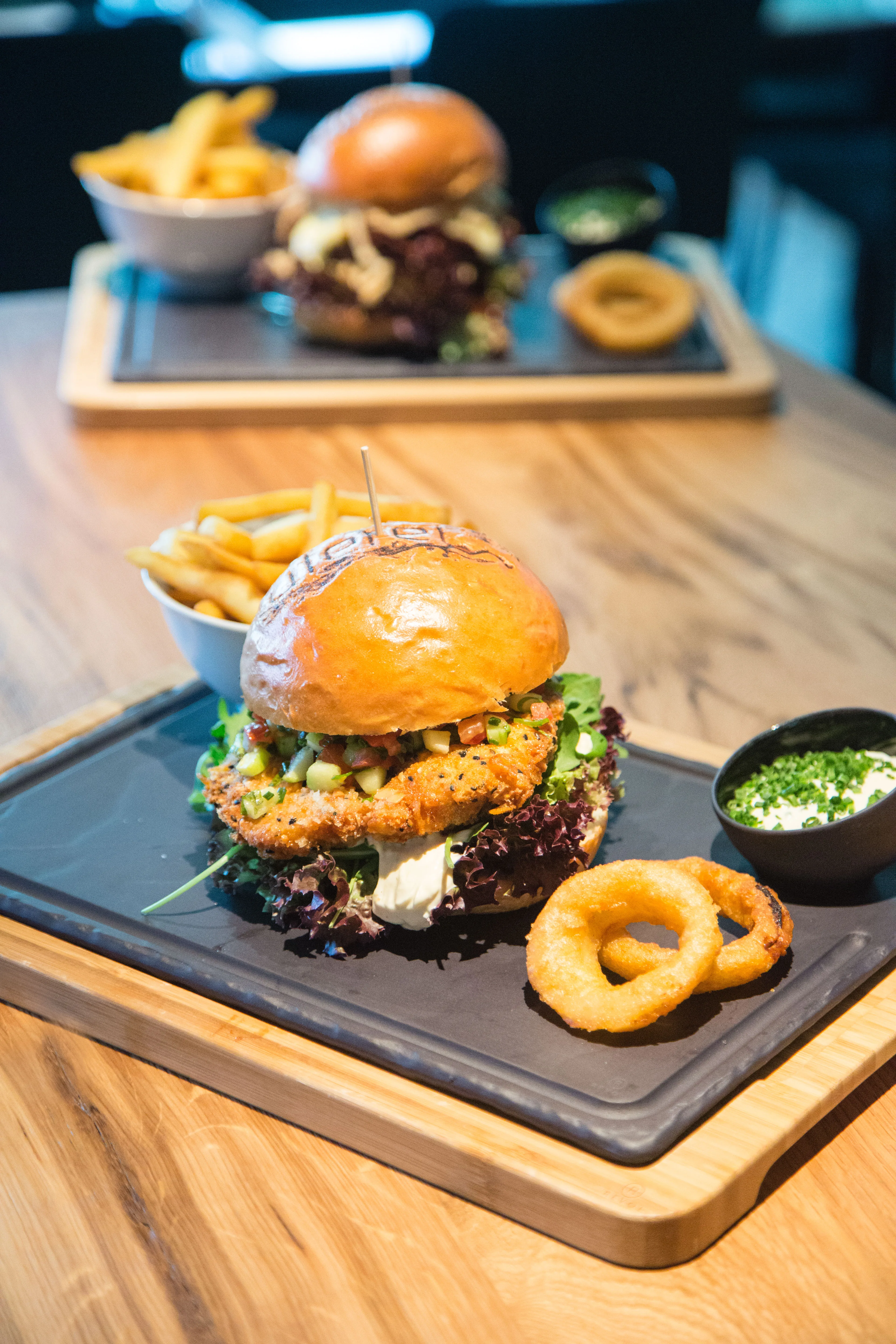 Ein saftiger Burger mit frischem Gemüse und Pommes auf einem Holzbrett.