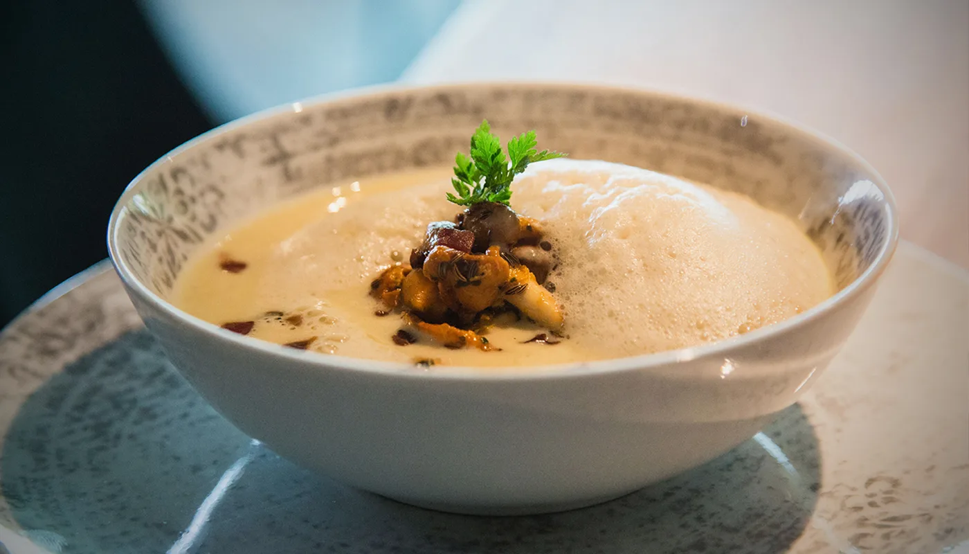 Eine kreative Suppe in einer Schüssel, garniert mit Kräutern und Pilzen.