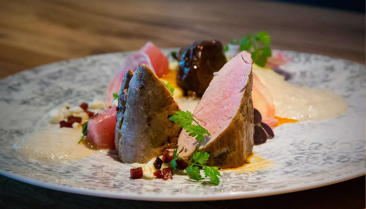 Ein kunstvoll angerichtetes Gourmetgericht mit zartem Fleisch und bunten Beilagen.