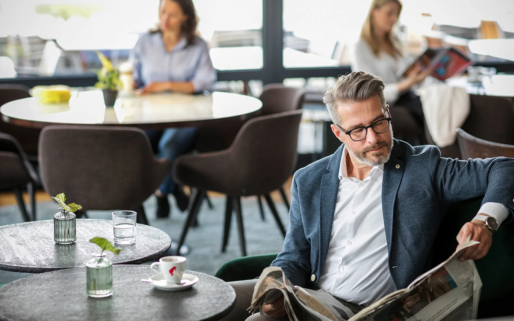 A man sitting in a modern café reading a newspaper.