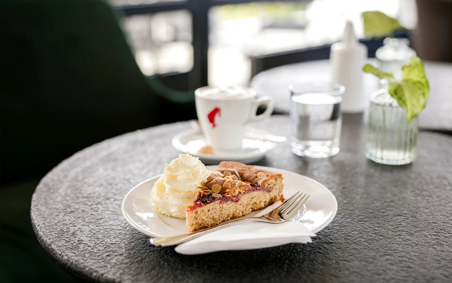 A piece of cake with cream and a cup of coffee on a table.